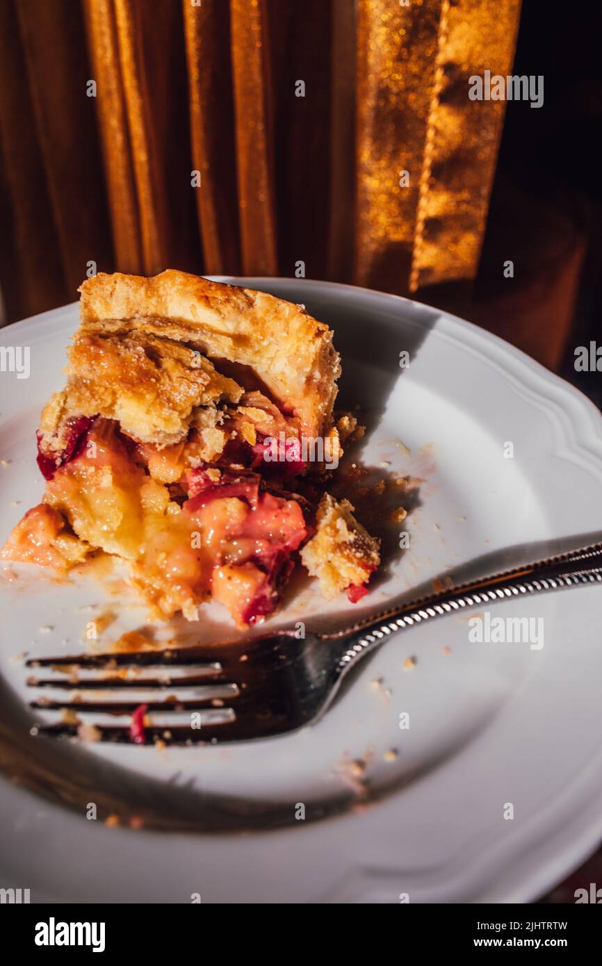 fetta metà mangiata di torta di crema al rabarbaro su piatto bianco con forchetta con sfondo dorato Foto Stock