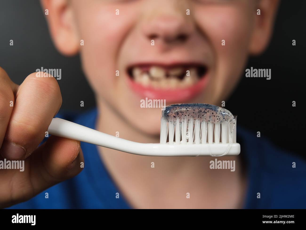Spazzolino da denti con dentifricio visto nelle mani di un bambino sorridente di 8 anni, senza denti. Concetto per la cura personale e l'igiene. Foto Stock