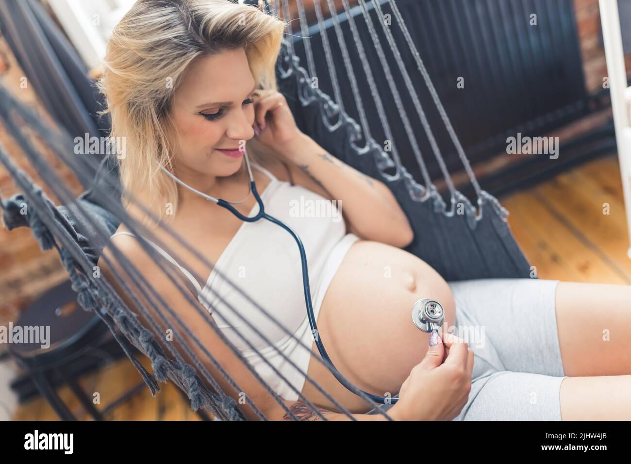 cowboy ha girato di una donna incinta nell'amaca ascoltando il battito del suo bambino con uno stetoscopio. Foto di alta qualità Foto Stock