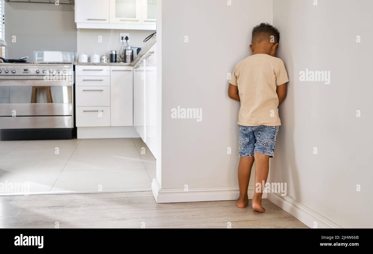 Pensando a quello che ha fatto, un ragazzino in piedi in un angolo a casa. Foto Stock