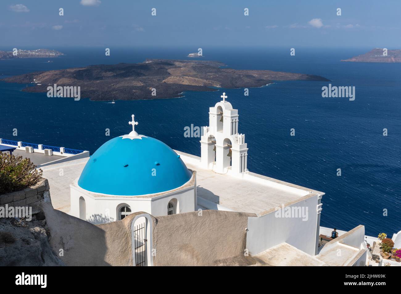 La Chiesa cattolica della Dormizione - tre campane di Fira con la sua cupola blu che si affaccia sul Mar Egeo e il vulcano, Fira, Santorini isola, Grecia Foto Stock