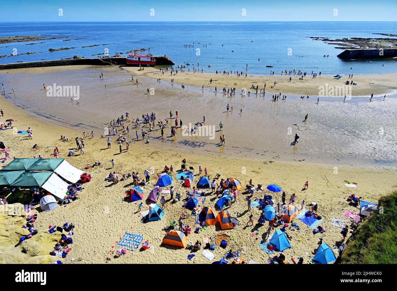 Cullercoats Bay Beach vista molte persone che si godono il sole con canoisti surf paddle boarders tende persone pic-nic barca da pesca presso la torta Foto Stock