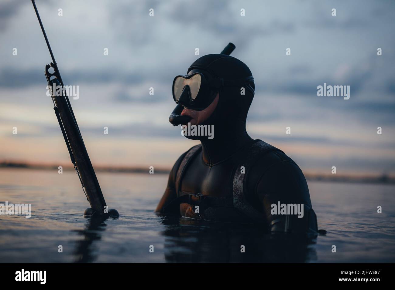 Uomo pesca d'altura con un fucile in mezzo al mare. Avventuroso pescatore a caccia di pesce indossando una maschera subacquea e una muta. Foto Stock