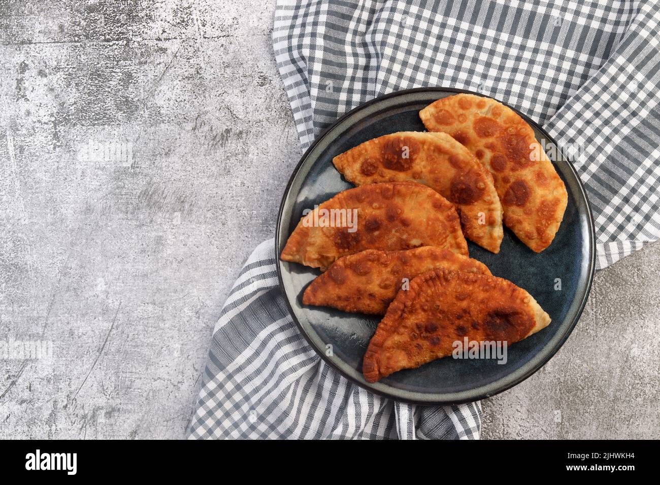 Chebureki - torte fritte in padella o turnover con carne e cipolla su un piatto rotondo su sfondo scuro. Vista dall'alto, piatto Foto Stock