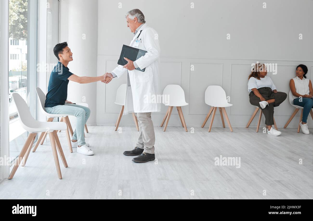 Un medico maturo che scuote le mani con un giovane nella sala d'attesa di una clinica. Foto Stock