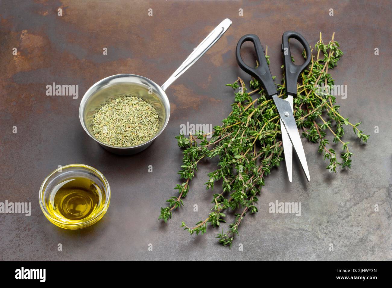 Ciuffi di timo verde e timo secco in ciotola metallica. Olio nel recipiente di vetro. Forbici su rametti di timo. Top Vew. Fondo in metallo arrugginito. Foto Stock