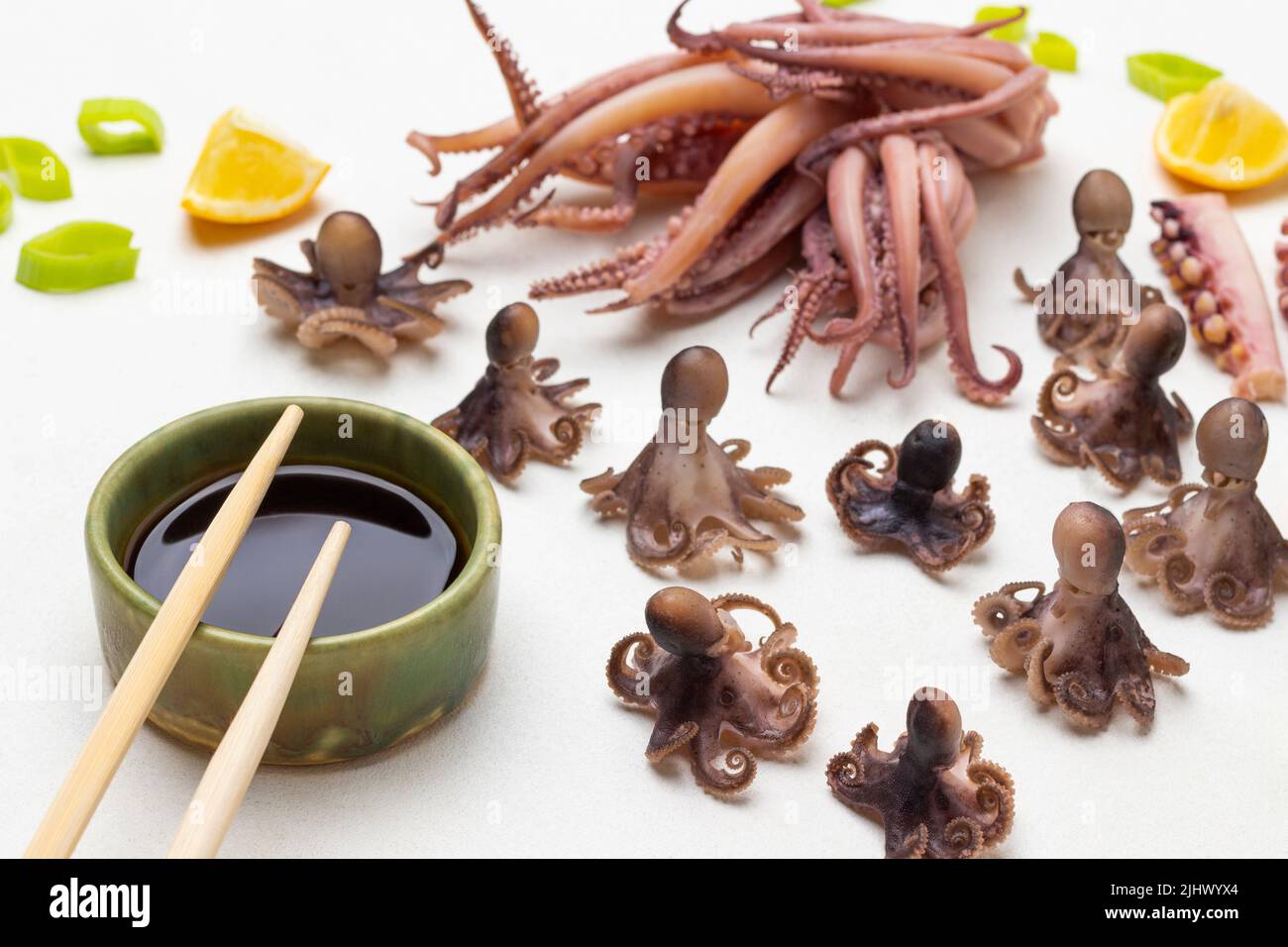 Salsa di soia in ciotola e bastoni di bambù. Bebè di polpo bollito e calamari con tentacoli sul tavolo. Vista dall'alto. Sfondo bianco Foto Stock