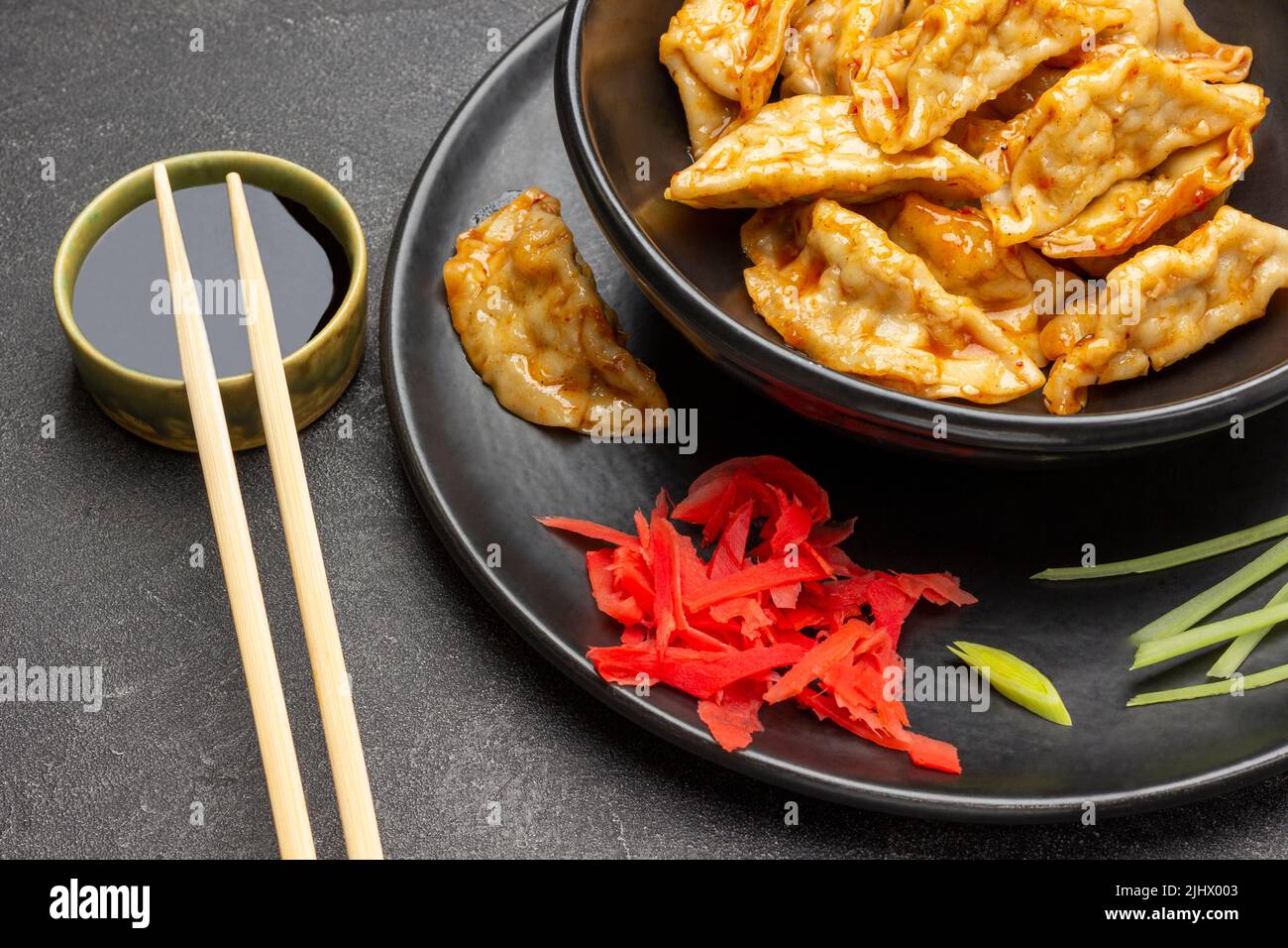 Gnocchi di gyoza fritti in salsa sul piatto nero. Salsa di soia in ciotola, bacchette. Vista dall'alto. Sfondo nero Foto Stock
