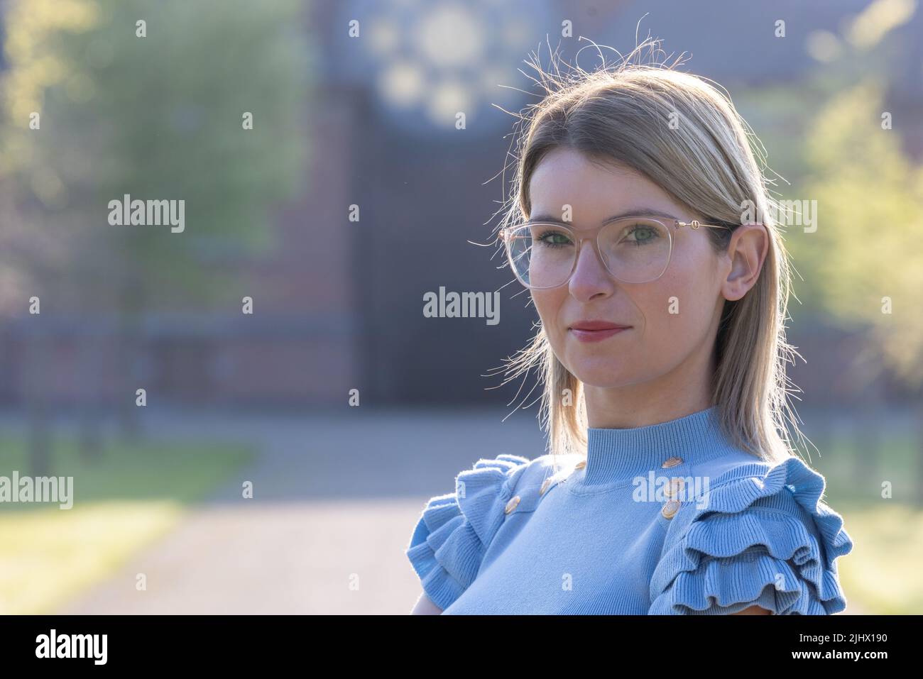 Affascinante modello giovane donna con occhiali e blusa blu in estate giorno di sole all'aperto e guardando lontano. Sottile caucasica bella ragazza a piedi nel parco. Foto di alta qualità Foto Stock