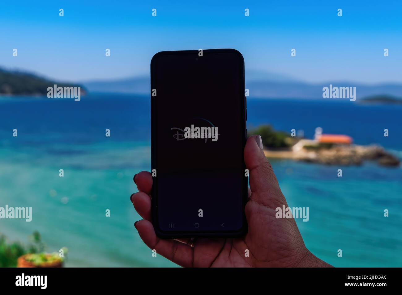 Femmina con telefono cellulare in mano, visualizza lo schermo con Disney+ streaming provider intro pagina sullo sfondo della spiaggia all'aperto. Foto Stock