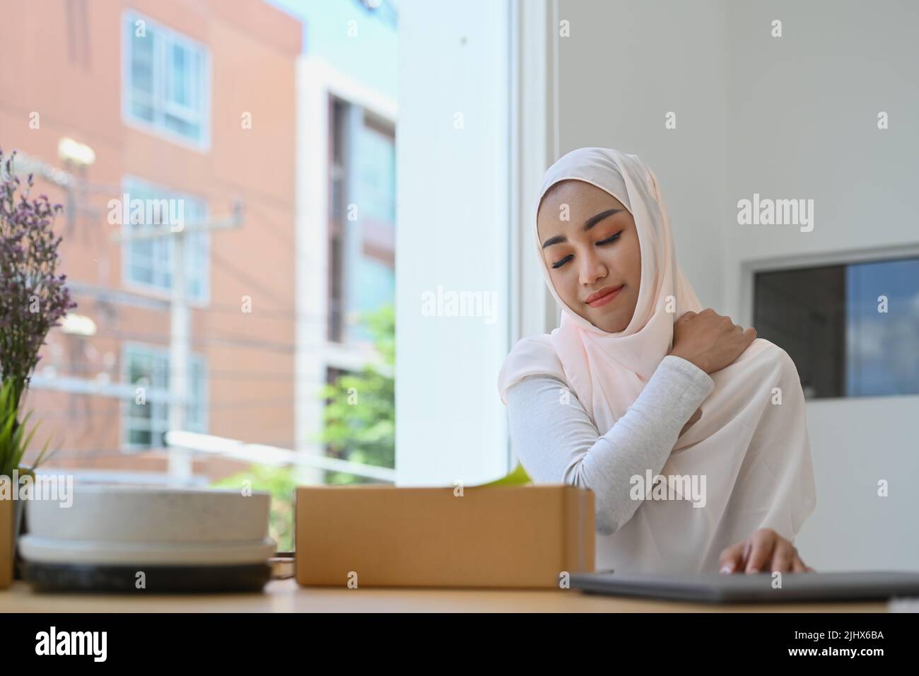 Donna d'affari musulmana sovraccarica massaggiando il collo rigido strofinando i muscoli tesi, che soffre di dolore al collo Foto Stock