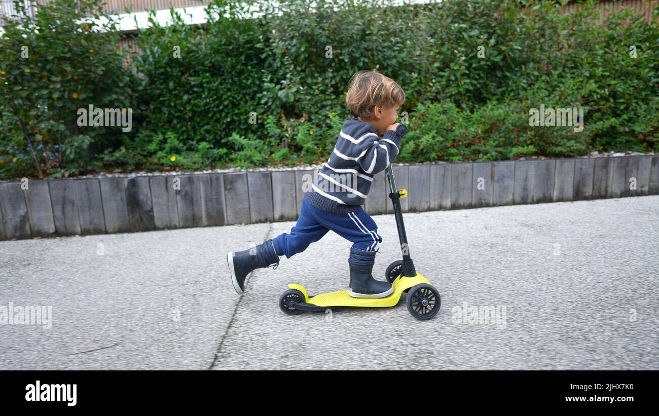 Ragazzino che guida tre scooter a ruote all'aperto Foto Stock