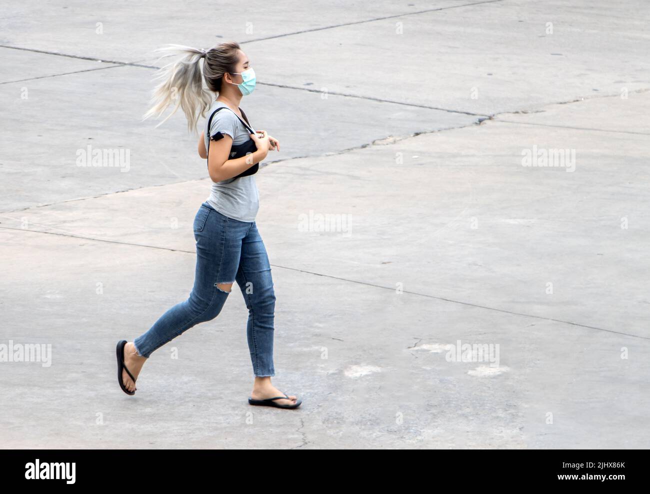 SAMUT PRAKAN, THAILANDIA, Apr 19 2022, Una giovane donna con una maschera sul suo volto sta correndo su una superficie di cemento in città Foto Stock