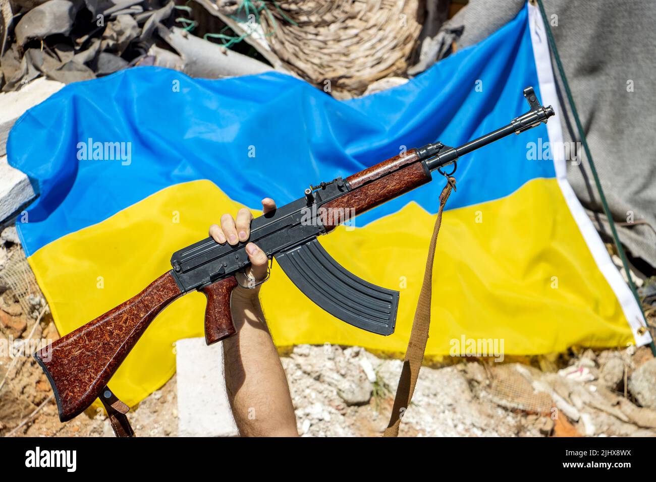 La pistola sollevata di fronte alla bandiera Ucraina sulle rovine Foto Stock