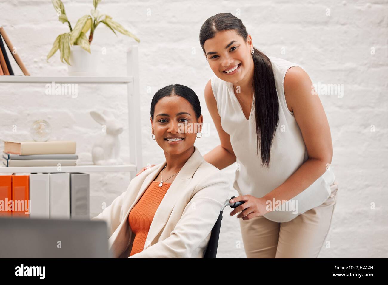 Ritratto di una giovane donna d'affari felice gara mista che aiuta un collega in sedia a rotelle al suo ufficio al lavoro. Contenuto ispanico businessperson con un Foto Stock