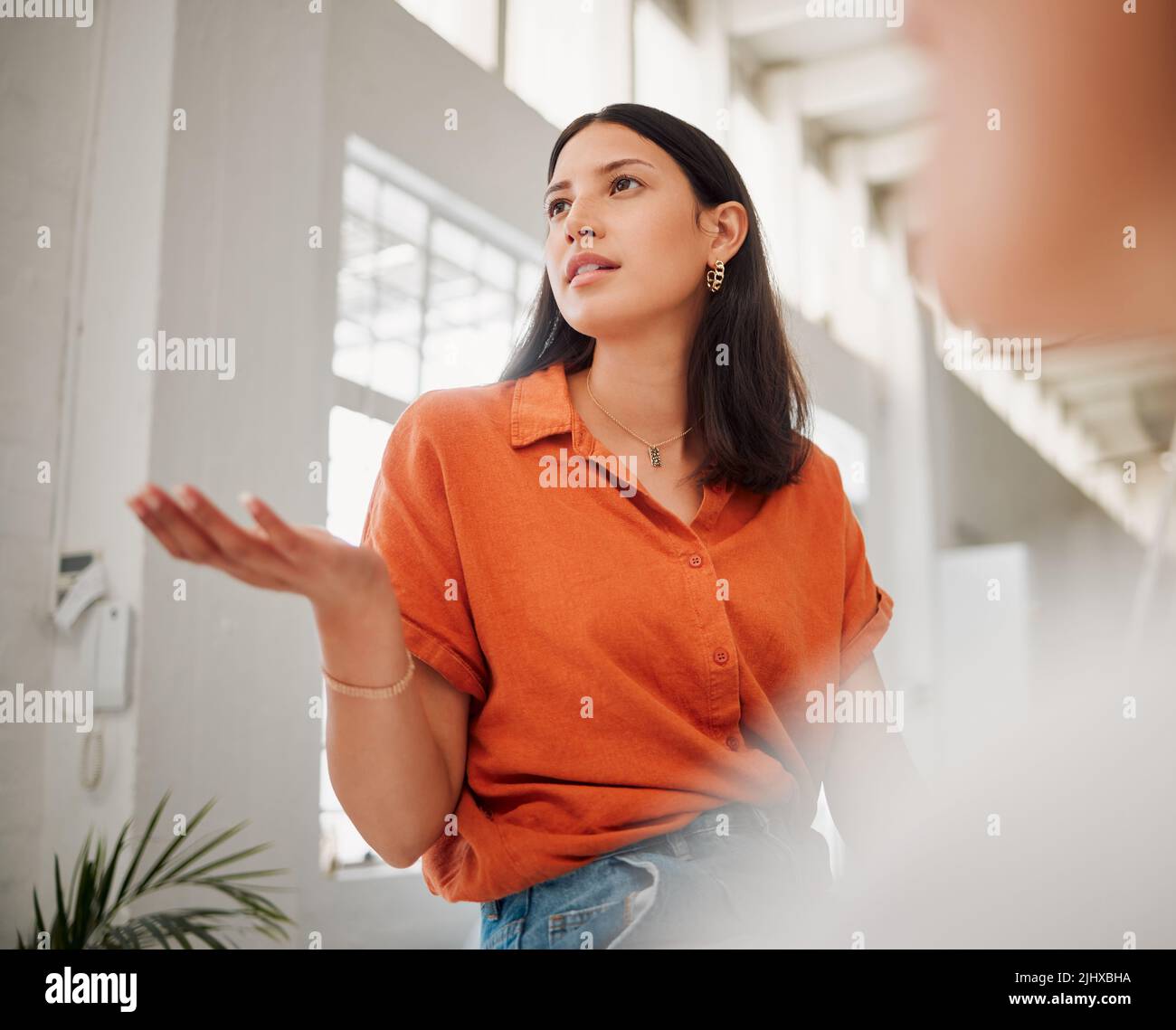 Giovane donna ispanica di sotto che parla con i colleghi durante una riunione in una sala riunioni d'ufficio. Donna che fa una domanda, condividendo il feedback e. Foto Stock