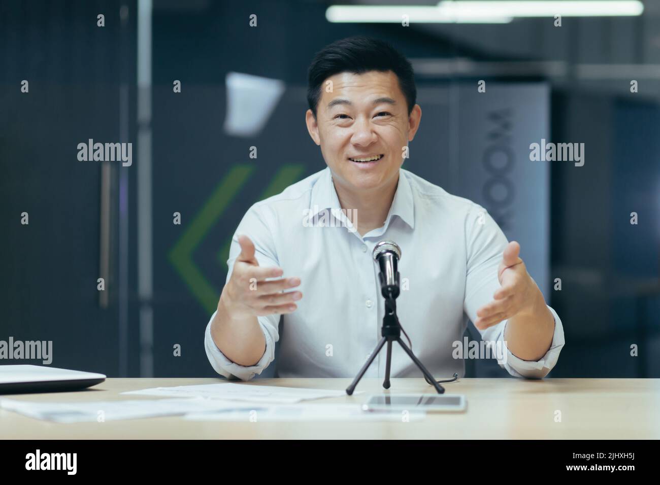 Primo piano ritratto fotografico di uomo d'affari che guarda in web camera e sorridente utilizzando microfono professionale per la comunicazione e la registrazione online podcast, business coach asiatico Foto Stock