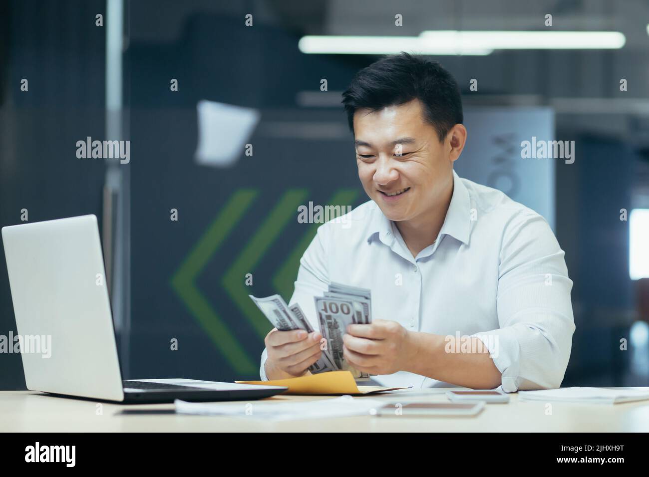 Riuscito investitore asiatico contando i dollari denaro in contanti seduta in ufficio, uomo felice sorridente e felice Foto Stock
