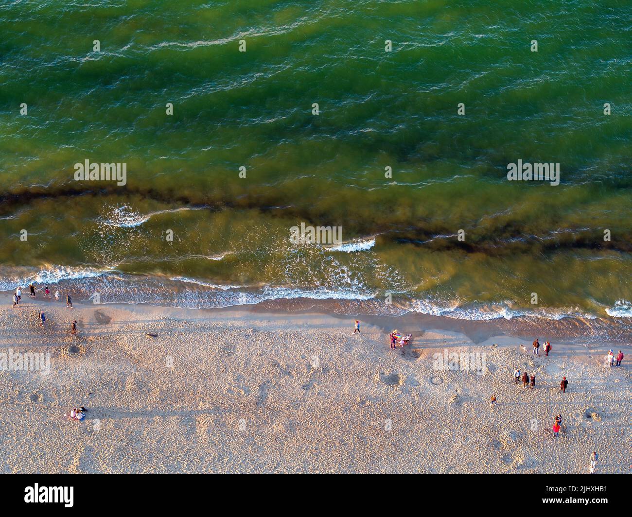 Persone che camminano sulla spiaggia da un mare smeraldo al tramonto, dall'alto verso il basso paesaggio al crepuscolo Foto Stock