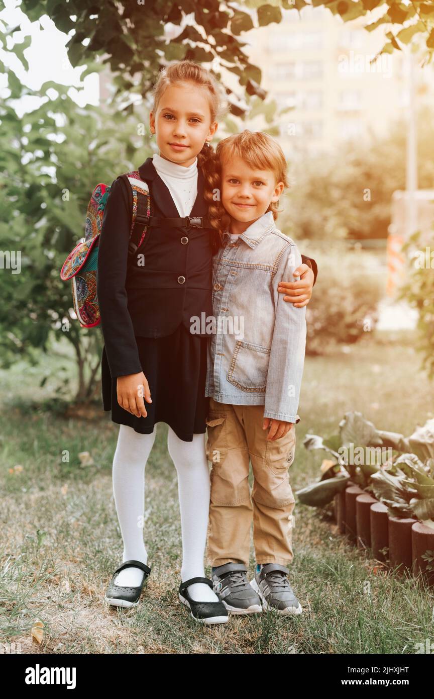 torna a scuola. bambina felice allievo studentessa otto anni in uniforme di moda con zaino e il suo fratello preschool ragazzo abbracciare insieme pronto andare Foto Stock