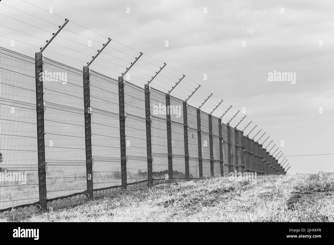 Recinzione di sicurezza con fili elettrificati lungo il confine della proprietà all'aperto in bianco e nero paesaggio. Foto Stock