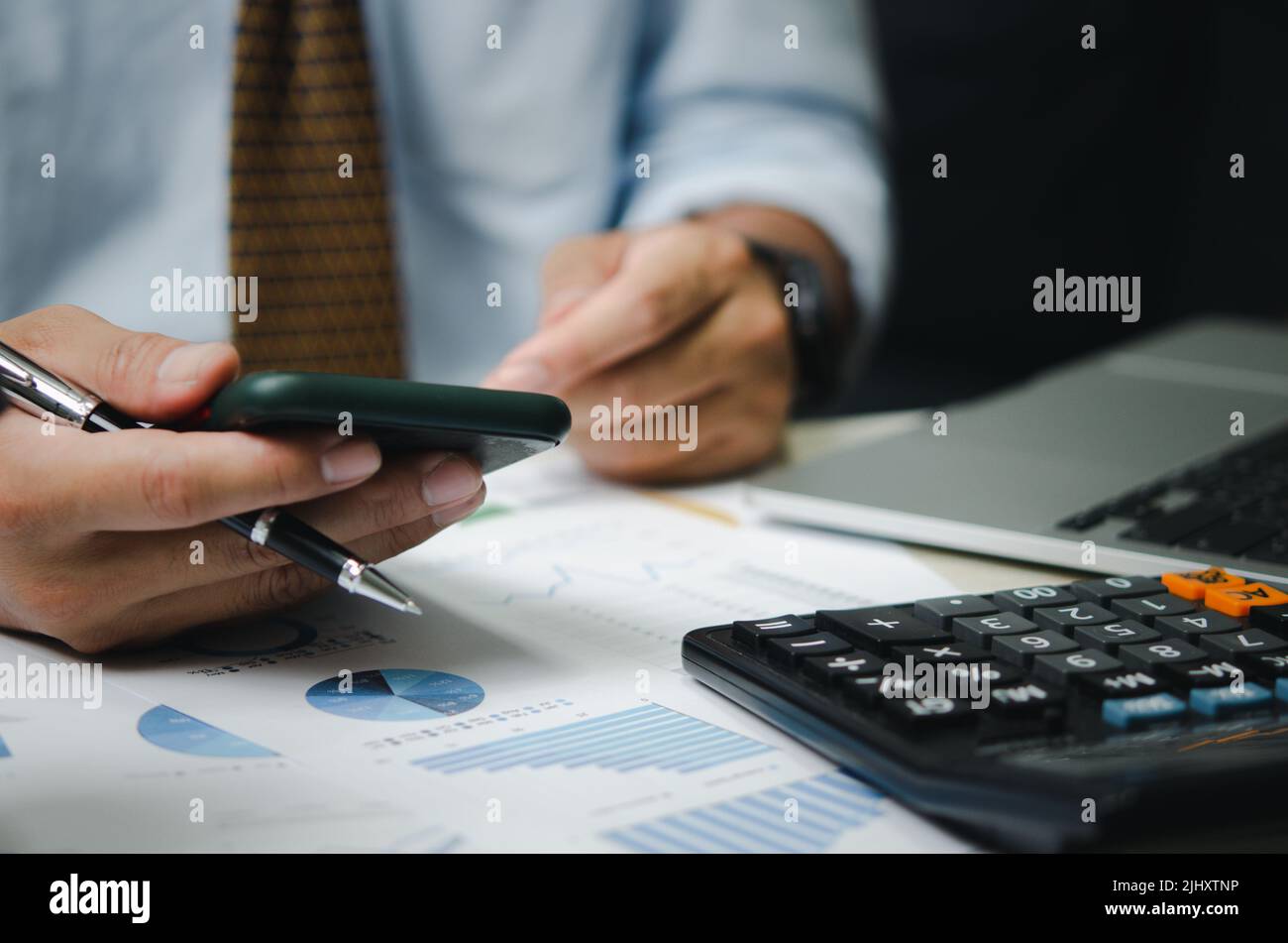 Uomo d'affari con telefono cellulare e penna con grafici e grafici documenti aziendali sulla scrivania. Calcolatore e computer per investimenti ed economici a Foto Stock