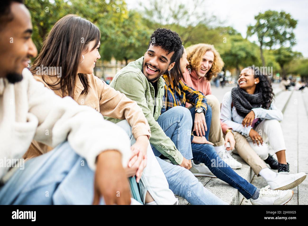 Gruppo felice di giovani alla moda che ridono insieme seduti all'aperto Foto Stock