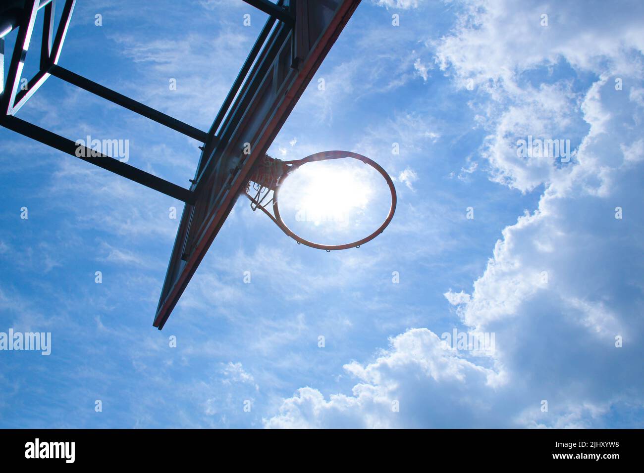 Anello di pallacanestro sullo sfondo un cielo blu con nuvole bianche e sole luminoso. Canestro da basket su uno scudo su un campo sportivo all'aperto. Pallacanestro Foto Stock