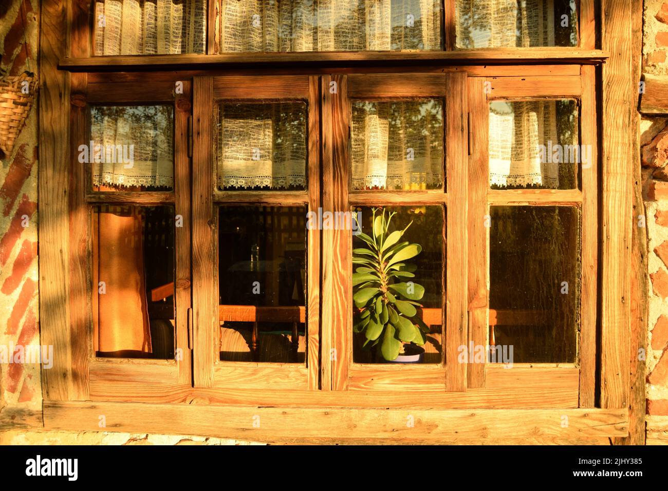 Finestre di una vecchia casa di villaggio tradizionale con cornici di legno, in legno e mattoni rossi, in luce solare dorata luminosa delle ore serali – primo piano esterno Foto Stock