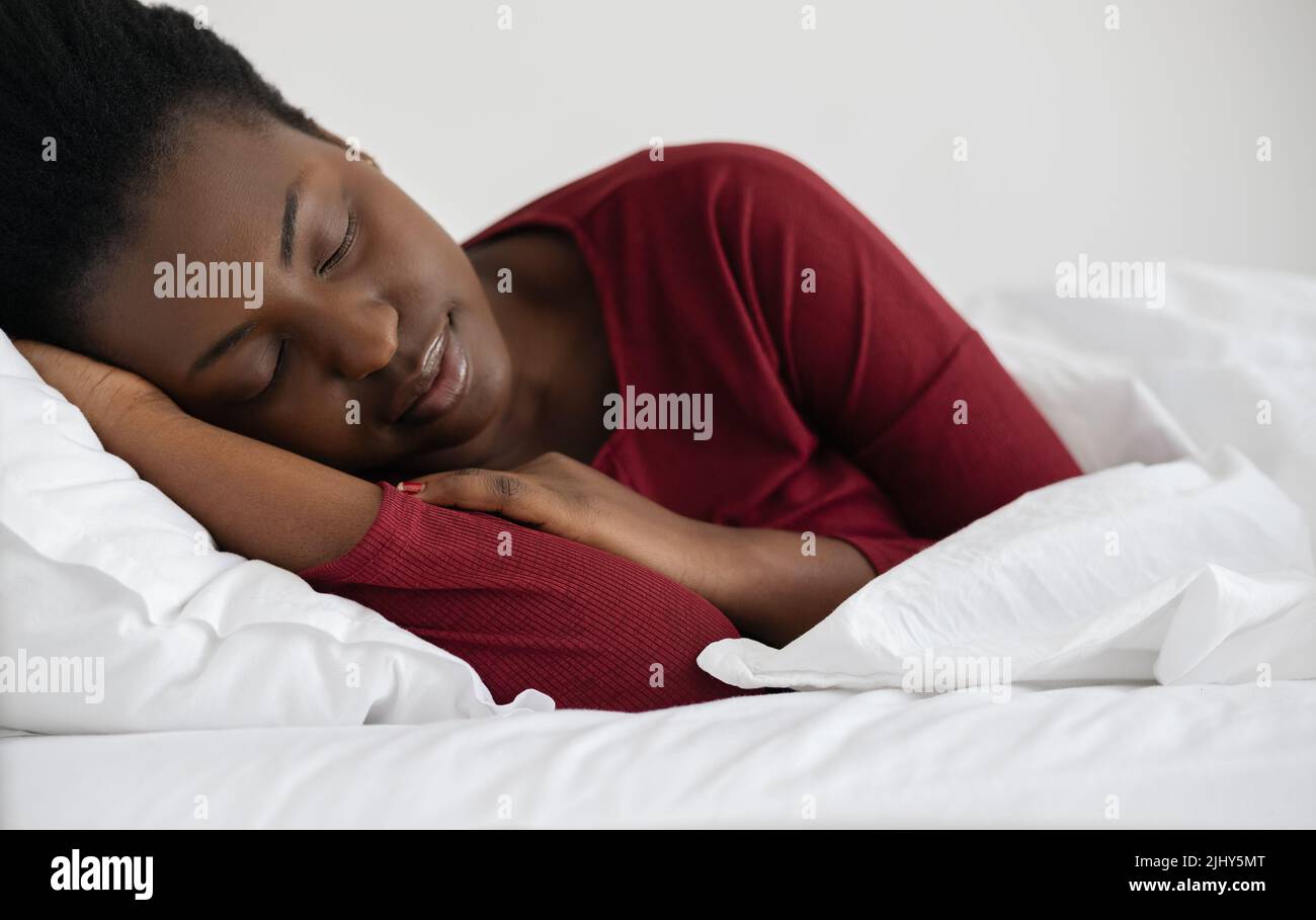 Giovane bella donna africana che dorme in letto di lino bianco, indossando pigiami rossi. Foto Stock