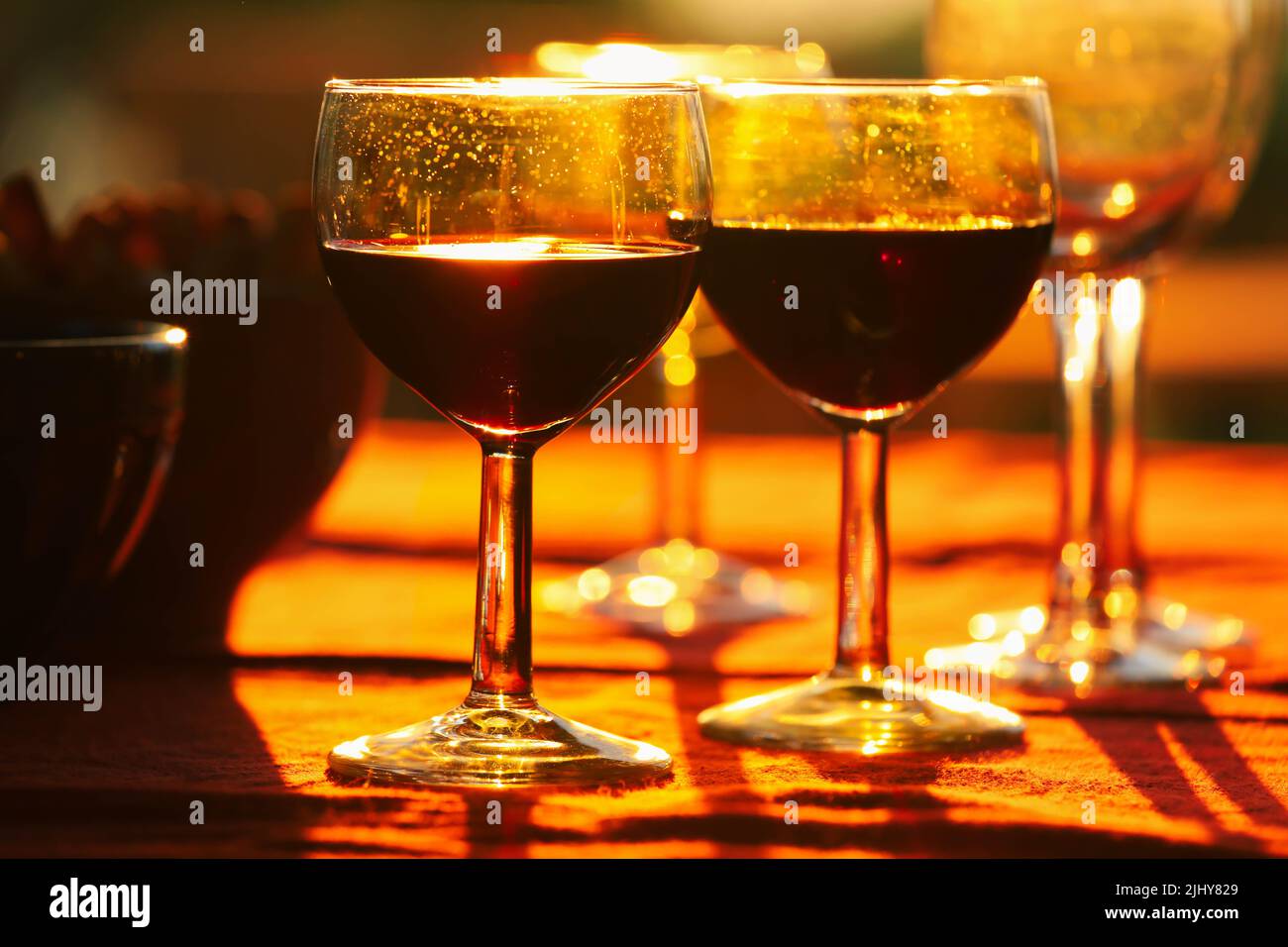 Bicchieri di vino rosso sul tavolo con spuntini sullo sfondo durante il tramonto Foto Stock