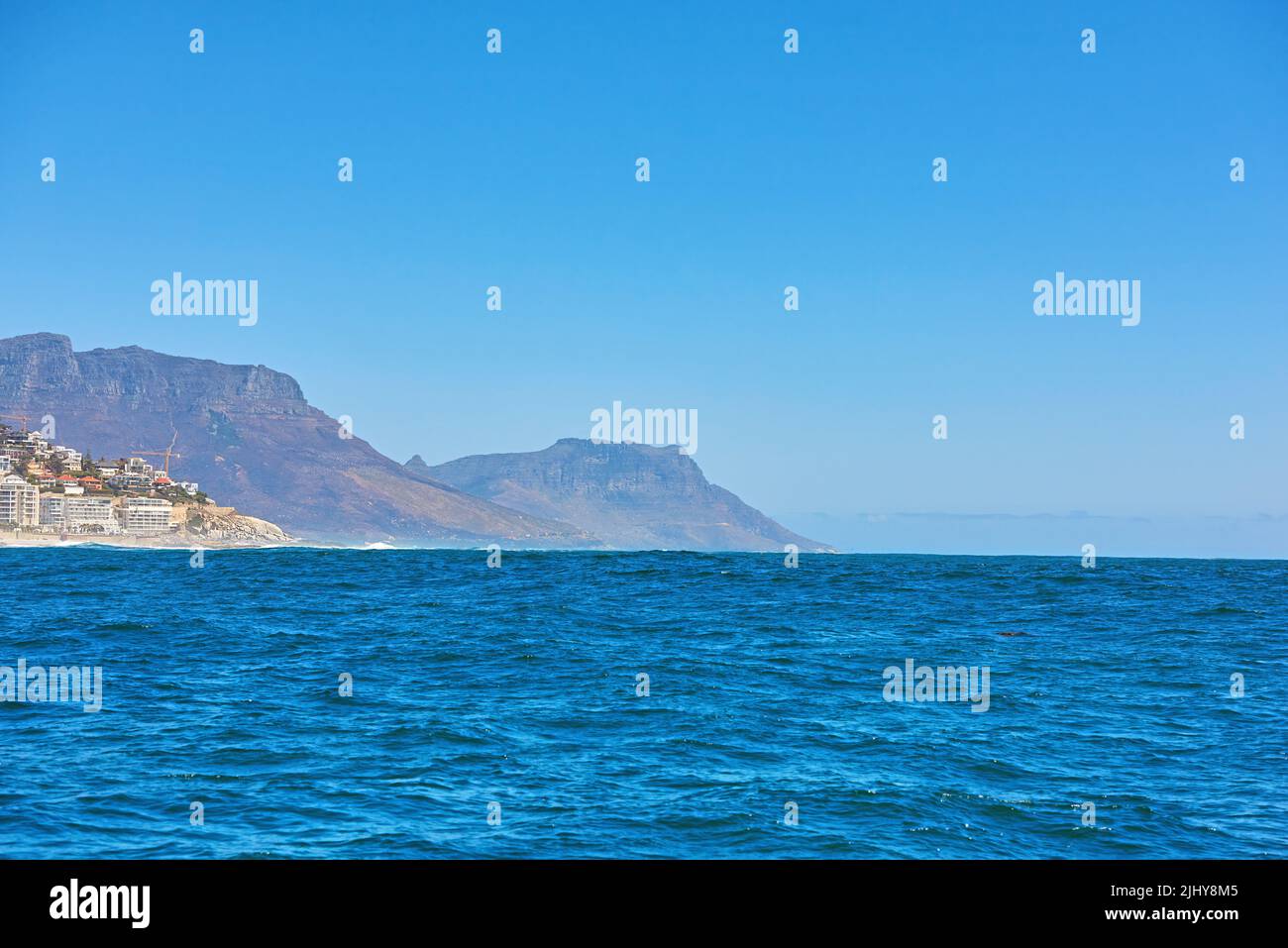 Il mare blu profondo o la vasta distesa dell'oceano aperto sotto il cielo blu chiaro copia spazio con Table Mountain sullo sfondo. Acque calme su un Foto Stock