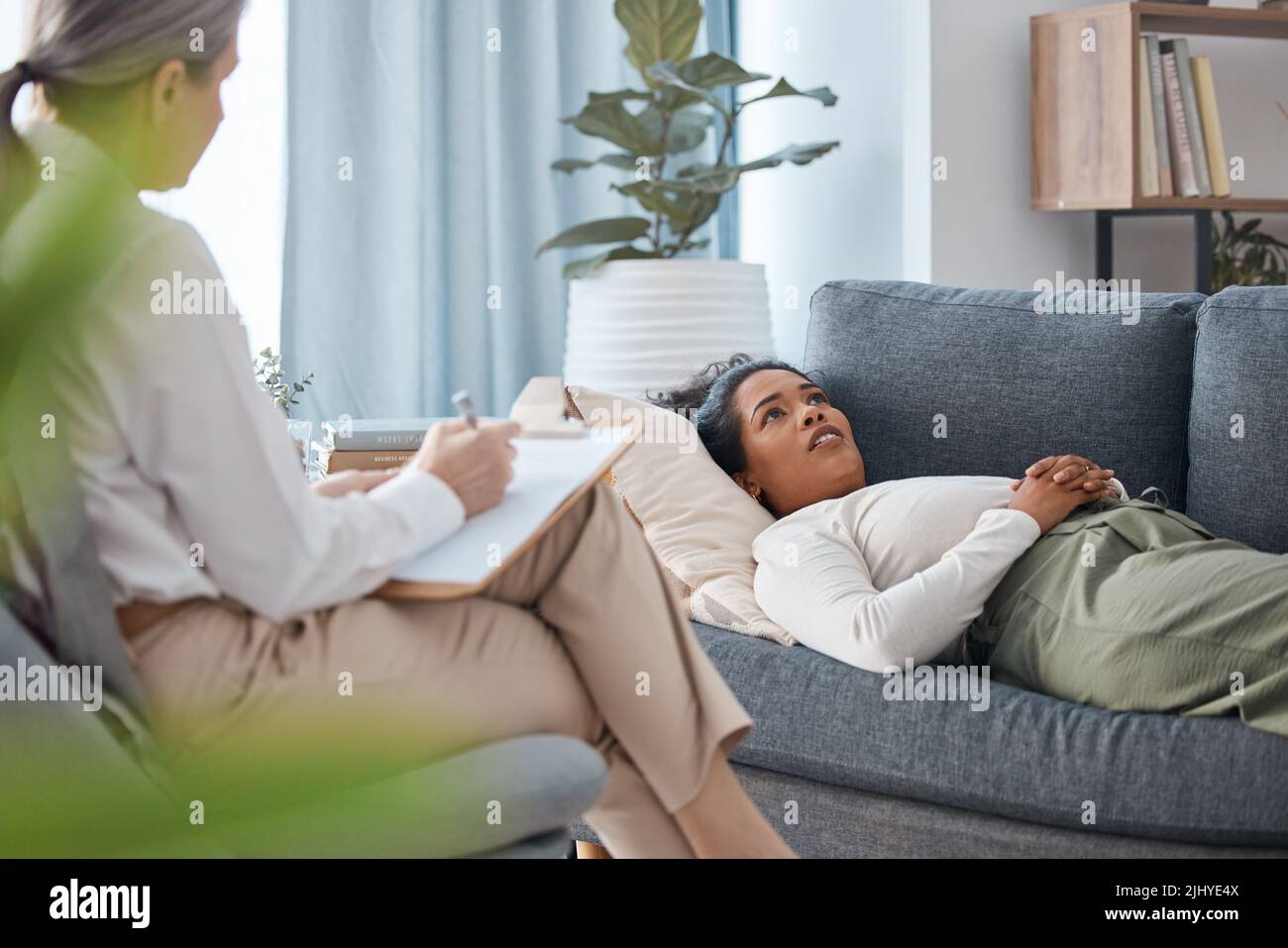 Il mio terapeuta sa tutto: Una giovane donna attraente che si distese e guarda contemplativa durante una consultazione con la sua psicologa. Foto Stock