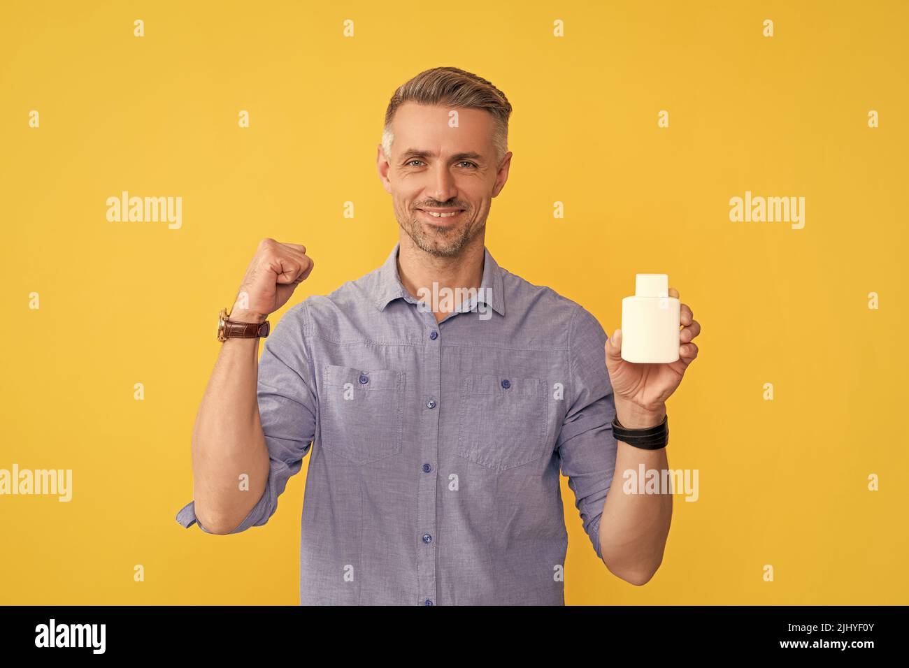 ragazzo felice che mostra la bottiglia di vitamina su sfondo giallo, supplemento Foto Stock