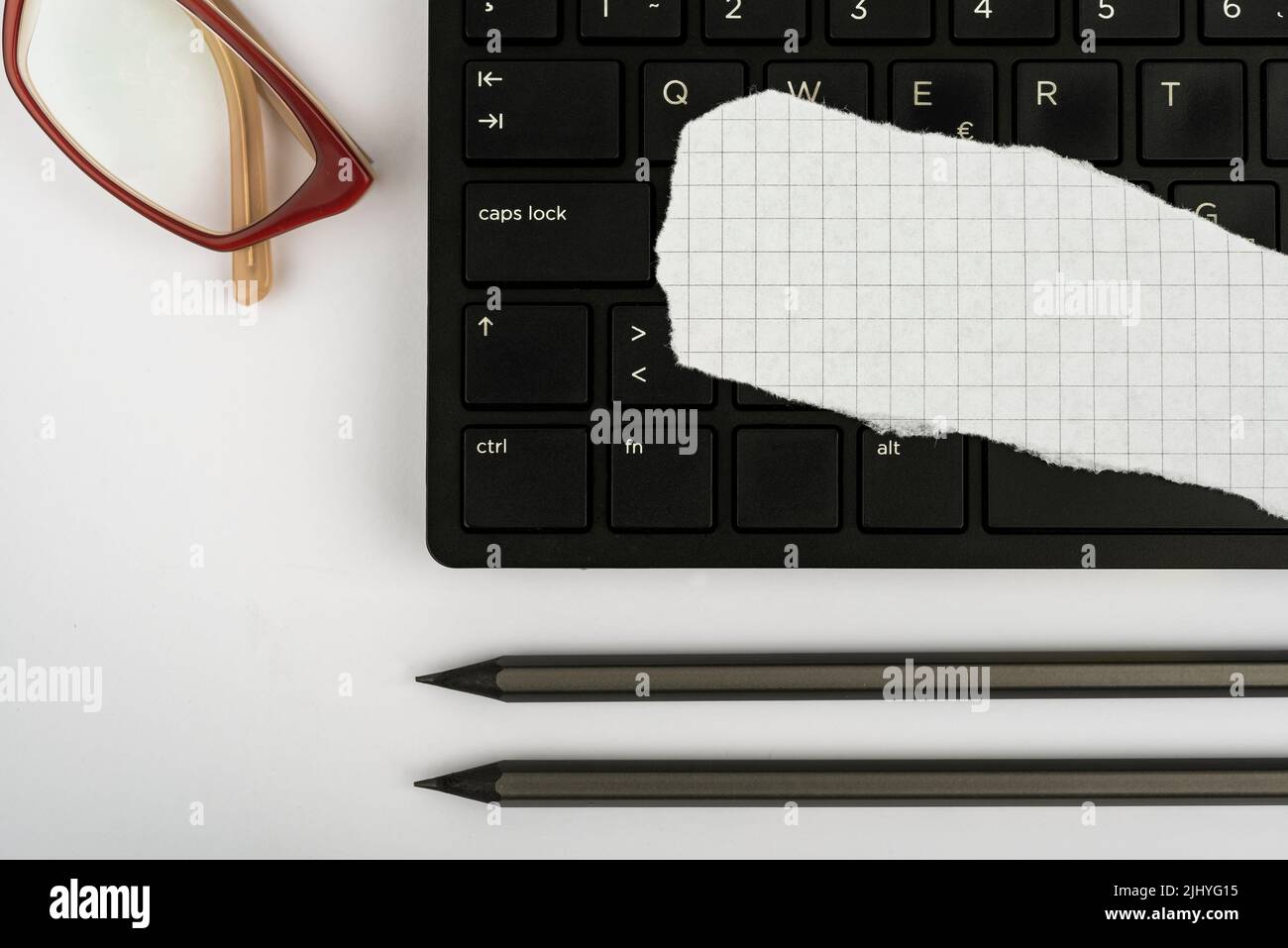 Una tastiera per computer, un pezzo di carta, matite e occhiali su un tavolo Foto Stock