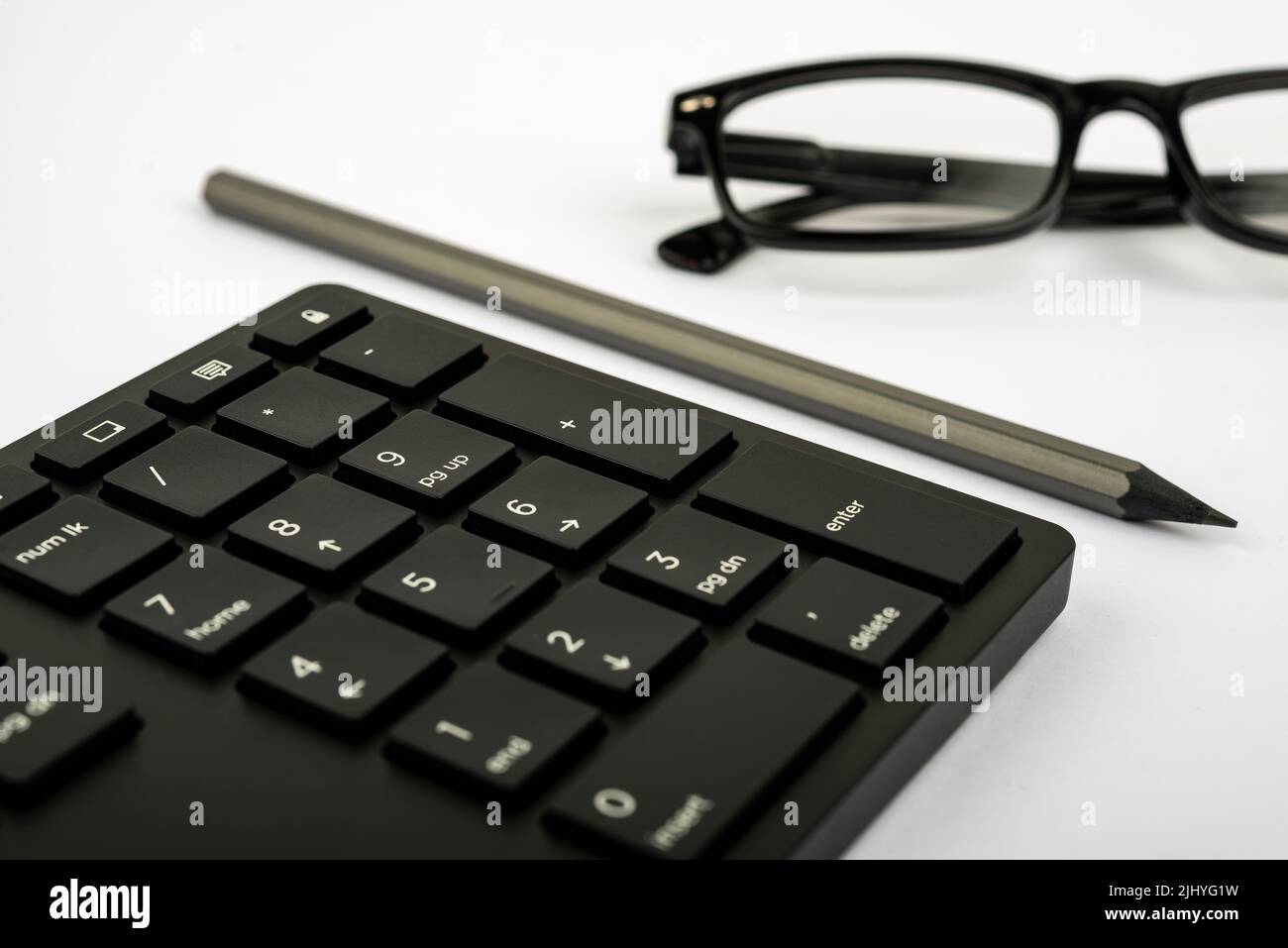 Una tastiera per computer, occhiali e una matita su un tavolo Foto Stock