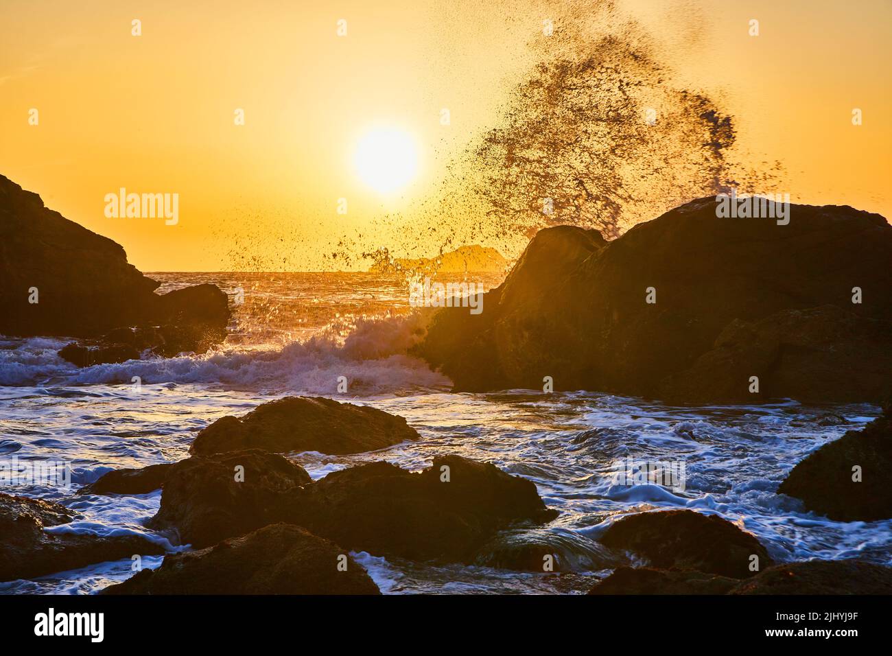 Le onde si infrangono in massi con il tramonto vibrante sulla costa occidentale Foto Stock