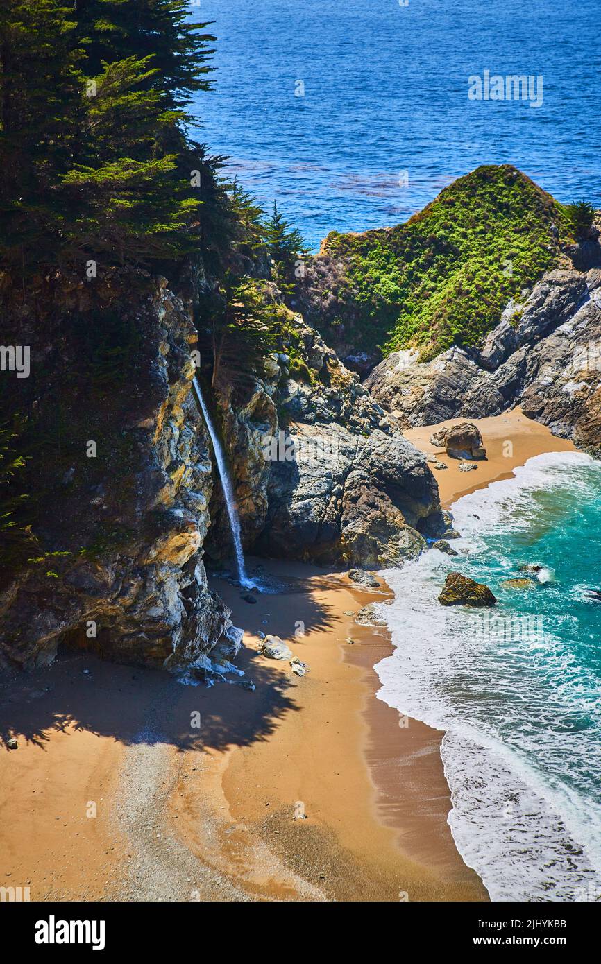 Vista della cascata nascosta dalle scogliere alle spiagge sabbiose dalle onde dell'oceano Foto Stock