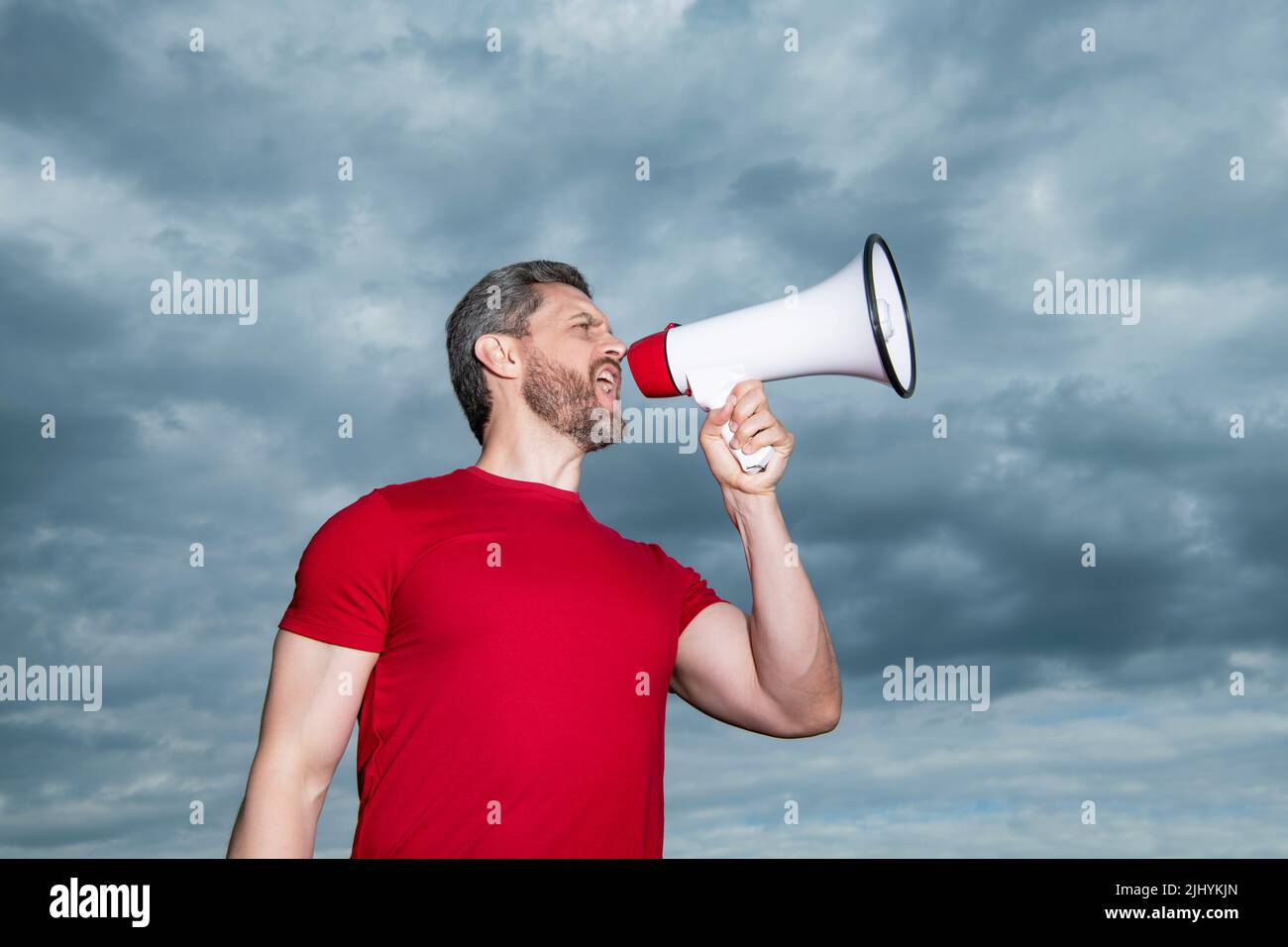 l'annunciatore in camicia rossa grida in altoparlante su sfondo cielo Foto Stock