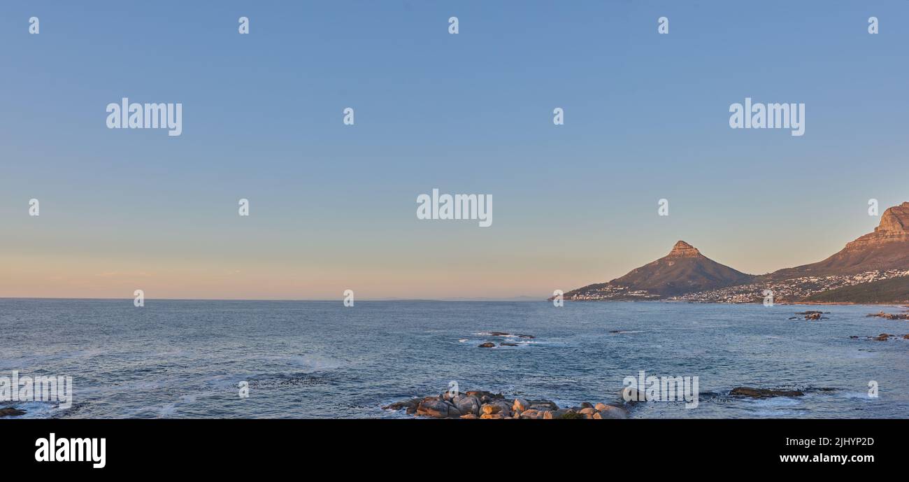 Splendida vista su un oceano tranquillo e montagne con un cielo blu sfondo e spazio copia. Paesaggio naturale mozzafiato del mare e orizzonte vicino Foto Stock