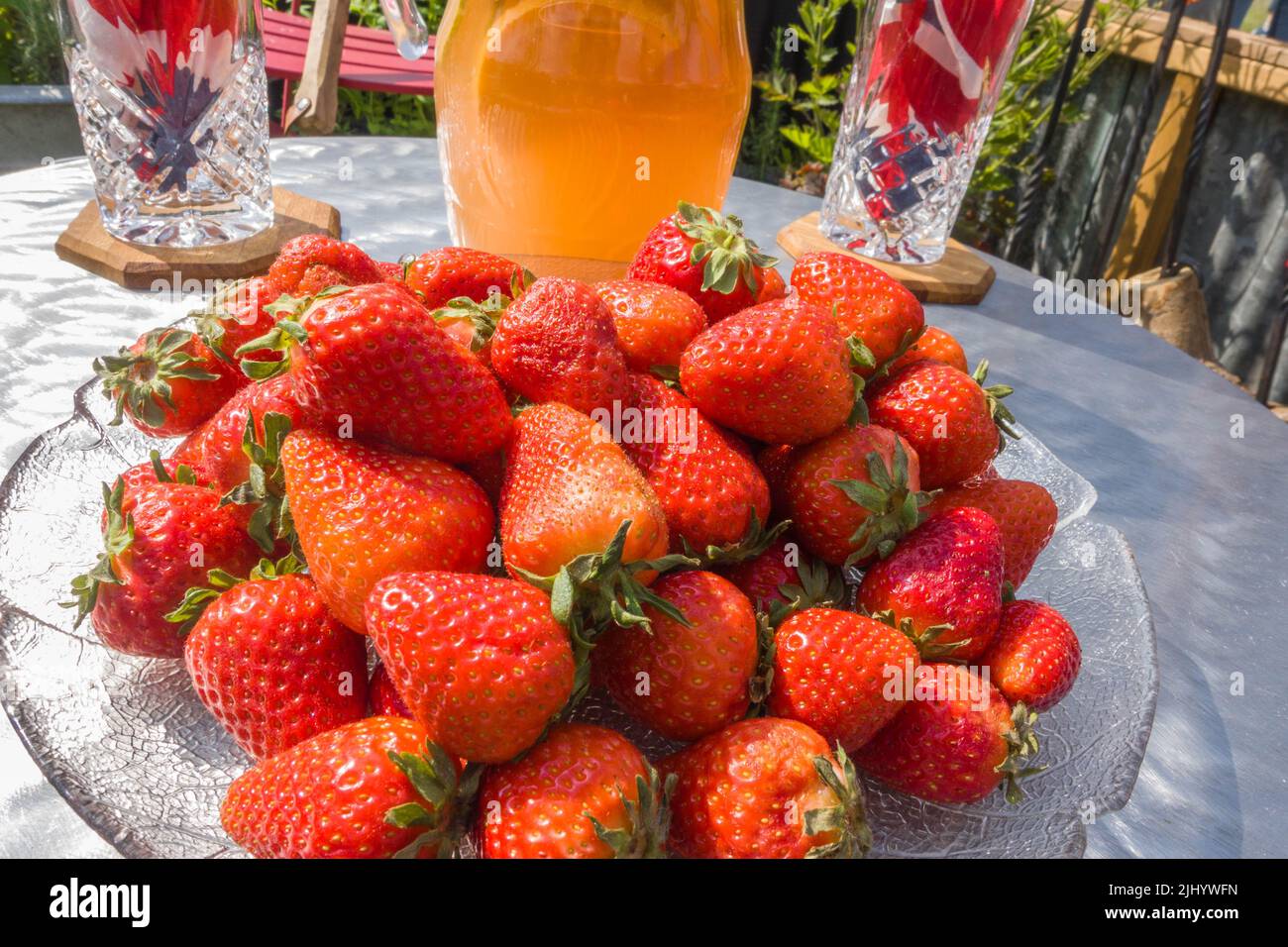 Piatto di vetro pieno di fragole fresche con succo di frutta e bicchieri sul retro Foto Stock
