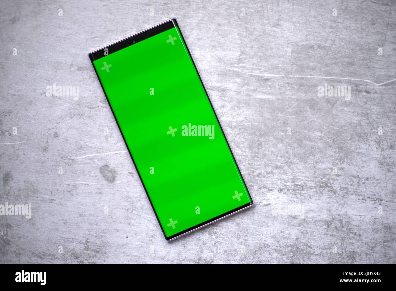 Lo smartphone è dotato di uno schermo verde vuoto per mockup come la demo di sviluppo di app o per l'uso nel design grafico. Il telefono cellulare si trova sul tavolo. Foto Stock
