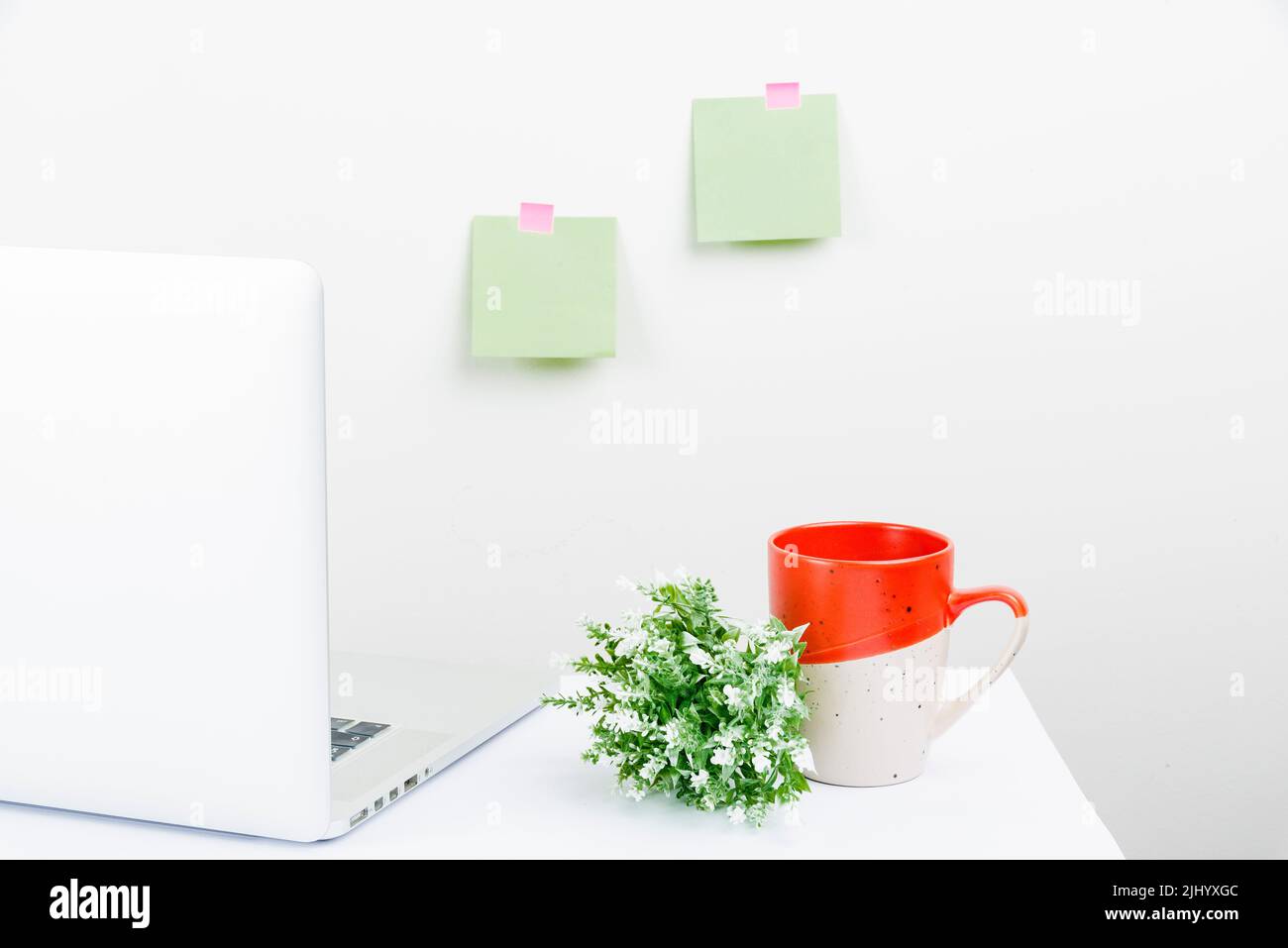 Un'area di lavoro bianca e ordinata con un computer portatile, note adesive, una tazza e una pianta Foto Stock