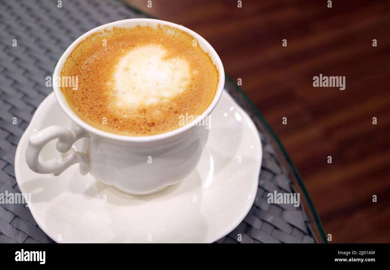 Una tazza di cappuccino con latte art a forma di cuore sul tavolo rotondo Foto Stock