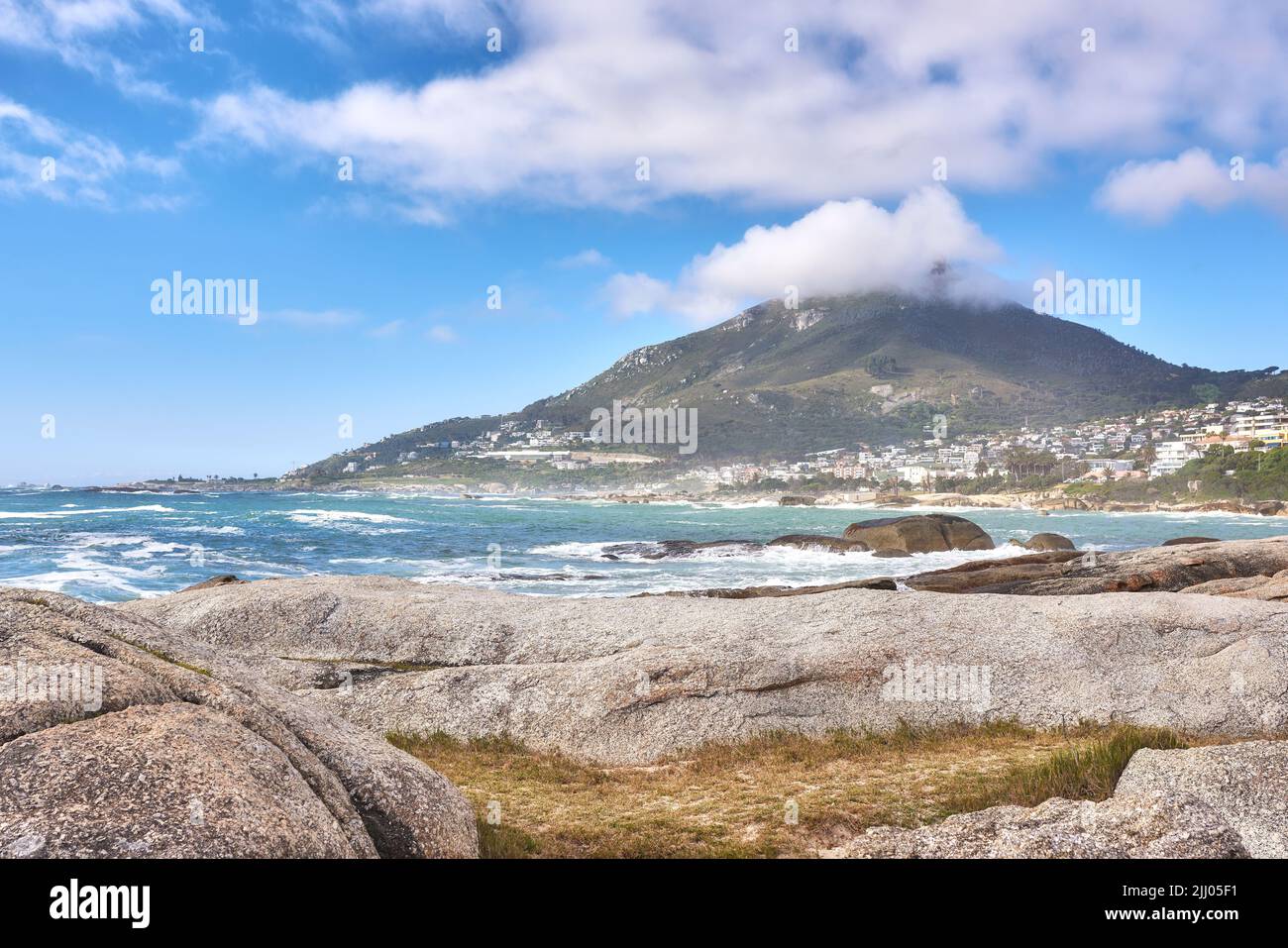 Bellissimo paesaggio di una spiaggia vicino a una montagna in una città costiera con un cielo blu nuvoloso in estate. Grandi rocce nel mare circondato dalla natura in un Foto Stock