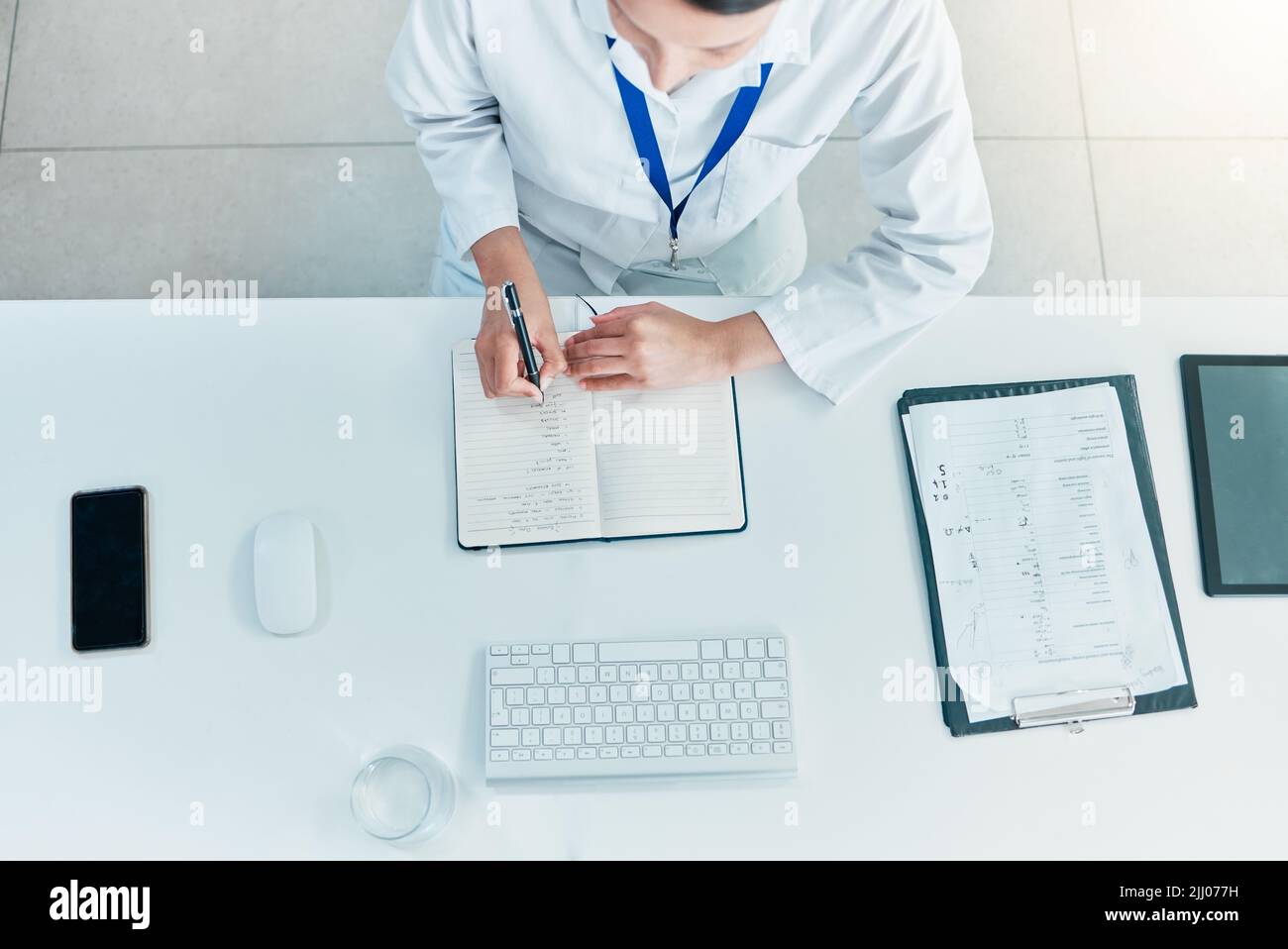 Lavorare il caso tutto il giorno. Scatto ad alta angolazione di uno scienziato irriconoscibile che scrive note mentre lavora su un computer in un laboratorio. Foto Stock