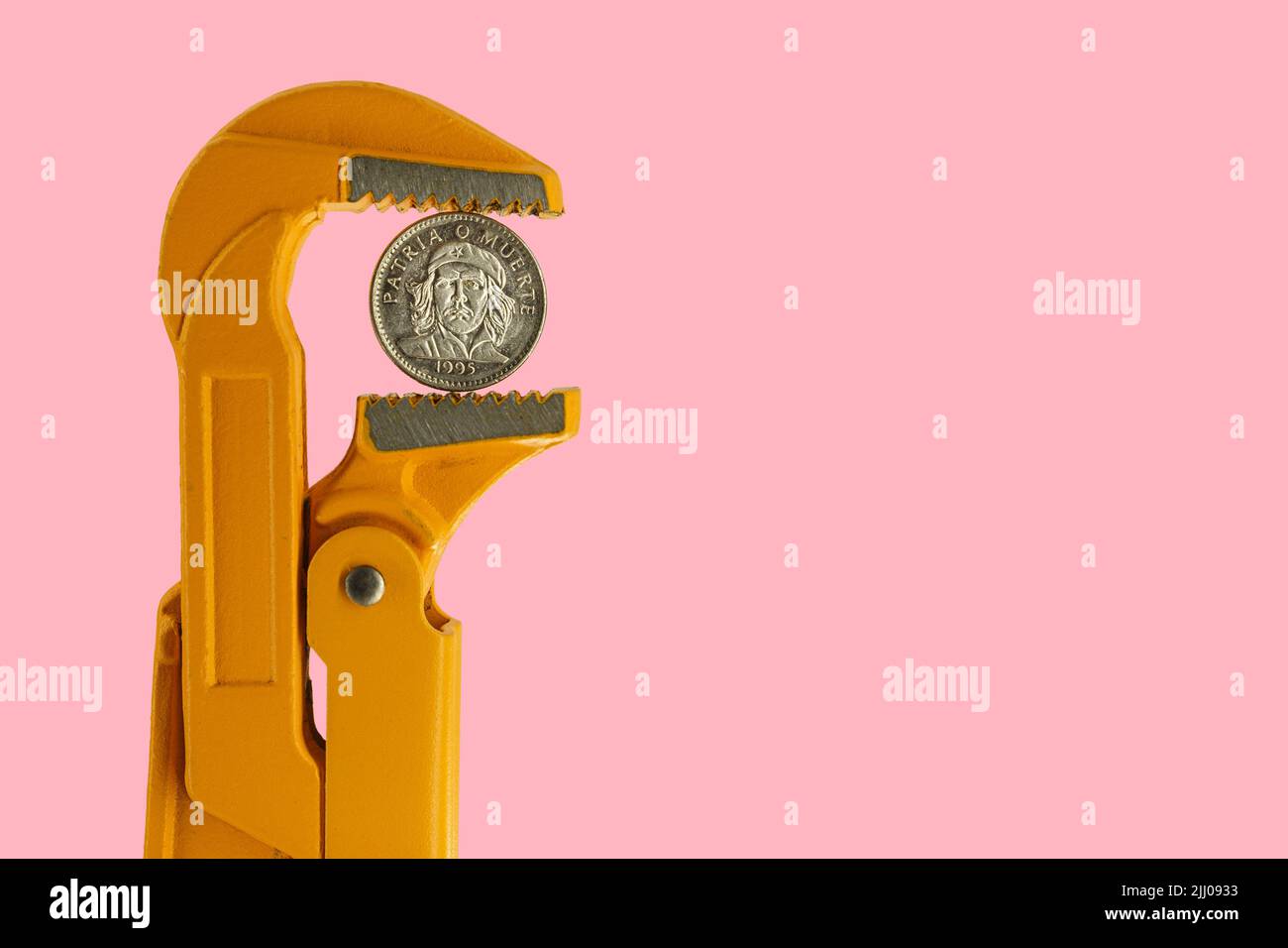 Tre monete cubane di peso tenute in una chiave per idraulico arancione su sfondo rosa Foto Stock