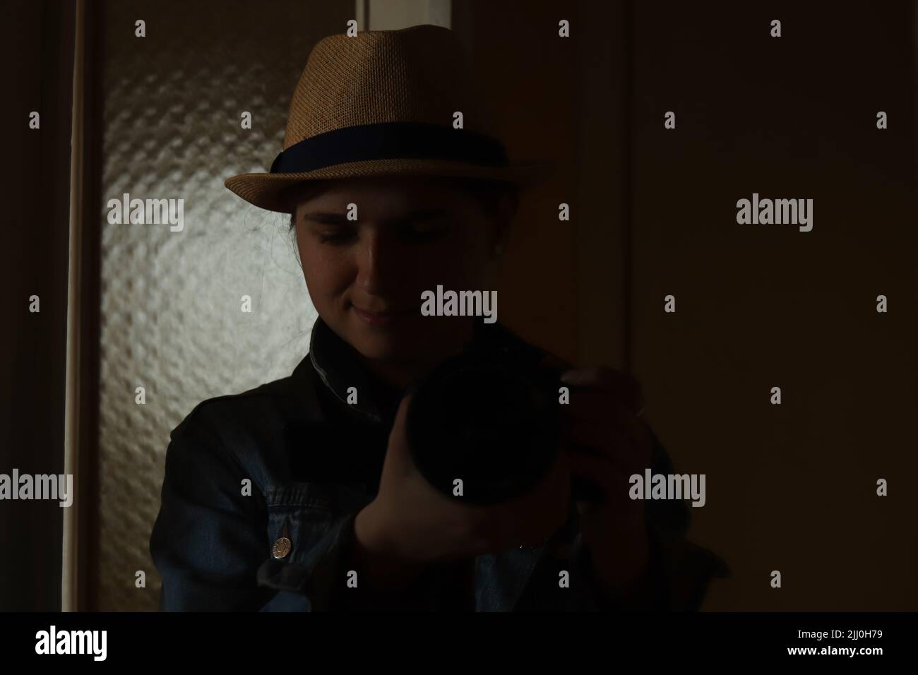 Defocus giovane donna prendere la fotografia in riflessione specchio. Donna millenaria in cappello. Ritratto nero scuro. Salute mentale. Narcisismo. Fotografo. Fuori Foto Stock