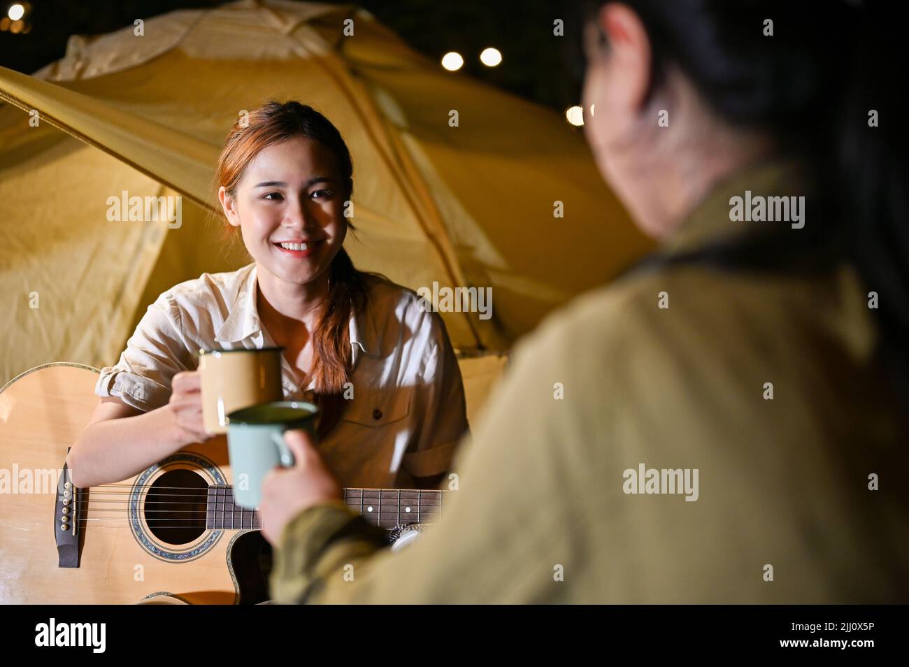 Bella giovane asiatica femmina godere di chiacchierare con i suoi amici, avendo una festa falò di notte nel campeggio. Foto Stock