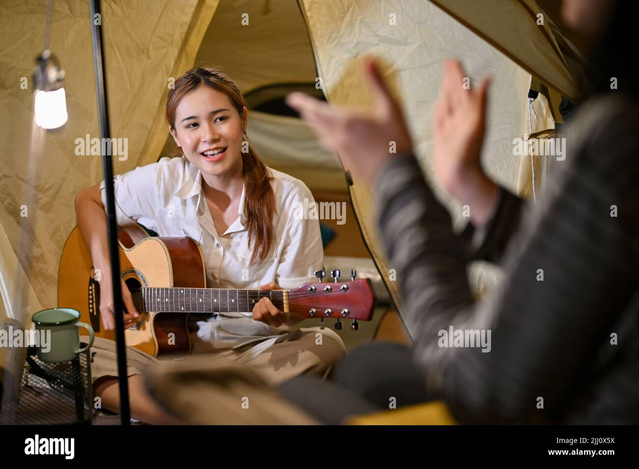 Affascinante giovane donna asiatica che suona la chitarra e canta con i suoi amici durante una festa di falò di notte nel campeggio. Attività all'aperto con Foto Stock